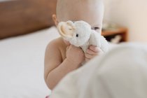 Baby girl sitting up in bed hiding behind soft toy — Stock Photo