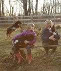 Mother and daughter outdoors, hugging goats and pet dog — Stock Photo