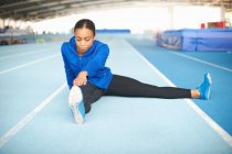 Jovem atleta feminina sentada no chão tocando os dedos dos pés — Fotografia de Stock
