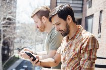 Male couple standing on balcony, looking at smartphones — Stock Photo