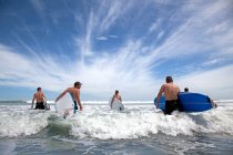 Groupe d'amis surfeurs masculins et féminins marchant dans la mer avec des planches de surf — Photo de stock