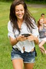 Дівчина-підліток дивиться на мобільний телефон під час прогулянки в сільській місцевості з друзями — стокове фото