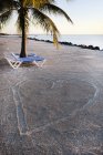 Espreguiçadeiras ao lado da forma do coração na superfície da praia arenosa — Fotografia de Stock