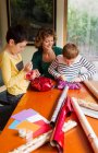 Donna e figli che avvolgono regali a tavola — Foto stock
