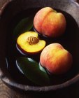 Ganze und halbe Pfirsiche und Blätter in einer hölzernen Schüssel mit Wasser — Stockfoto