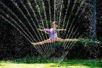 Ballerina leaping through a water sprinkler — Stock Photo