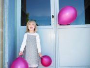 Porträt eines Mädchens, das mit rosa Luftballons vor der Tür steht — Stockfoto