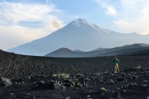 Uomo in piedi in campo di lava con Vulcano Tolbachik sullo sfondo, penisola di Kamchatka, Russia — Foto stock