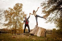 Young couple playing on tree stump in autumn park — Stock Photo