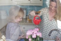 Мать и дочь моют посуду, мать наливает воду — стоковое фото
