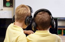Dos chicos de la escuela usando auriculares, mirando la pantalla de la computadora - foto de stock
