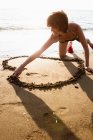 Woman drawing heart in sand on beach — Stock Photo