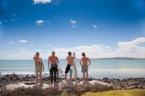 Quatro jovens surfistas amigos assistindo mar de rochas — Fotografia de Stock
