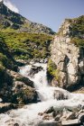 Water flowing down rocks to river in bright sunlight — Stock Photo