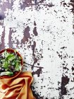 Stillleben von Salatblättern in Schüssel und orangefarbener Serviette auf rustikalem Tisch — Stockfoto