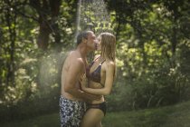 Mature homme et jeune copine embrasser sous la douche du jardin — Photo de stock