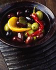 Зелені та чорні оливки, червоний чилі, апельсиновий шматочок у дерев'яній мисці — стокове фото