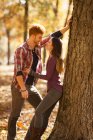 Romantic young couple leaning against tree in autumn forest — Stock Photo