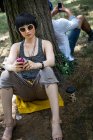 Junge Frau lehnt mit MP3-Player an Baumstamm — Stockfoto
