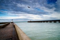 Harbor wall and wooden pier under cloudy sky — Stock Photo
