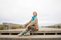 Donna seduta sulla passerella sulla costa — Foto stock