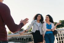 Two mid adult women greeting male friend on waterfront — Stock Photo