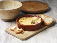 Bowl of welsh rarebit bake with toasted bread on wooden chopping board — Stock Photo