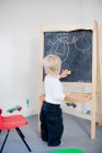 Back view of small Boy drawing on blackboard — Stock Photo