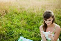 Молодая женщина смотрит на ручное устройство в поле — стоковое фото