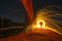 Silhouetted person creating yellow circular light trails on arch rock formation at night, Utah, USA — Stock Photo
