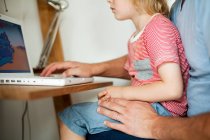 Garçon assis sur les genoux du père au bureau informatique — Photo de stock