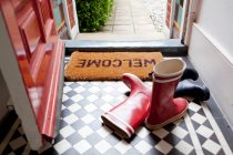 Welcome mat and wellington boots on doorway — Stock Photo