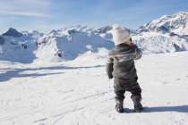 Молодий хлопчик стоїть, дивлячись на гори в снігу — стокове фото