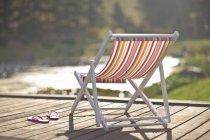 Deckchair and pair of flipflops on river pier — Stock Photo