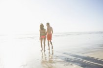 Rear view of young couple in swimwear strolling on sunlit beach, Cape Town, Western Cape, South Africa — Stock Photo