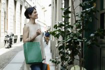 Mujer con bolsas de compras menú de lectura fuera del restaurante, Milán, Italia - foto de stock