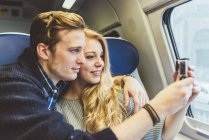 Parejas jóvenes fotografiando a través de la ventana del vagón de tren, Italia - foto de stock