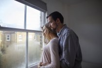 Mid casal adulto olhando para fora através da janela do quarto — Fotografia de Stock