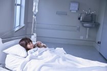 Menina paciente na cama abraçando brinquedo coelho na enfermaria de crianças do hospital — Fotografia de Stock
