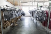 Sewing patterns and garments hanging on clothes rails in sewing factory — Stock Photo