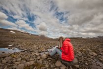 Feminino turista sentado em paisagem rochosa escrevendo em notebook, Seyoisfjorour, Islândia — Fotografia de Stock