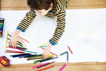 Overhead view of boy lying on floor drawing on long paper — Stock Photo
