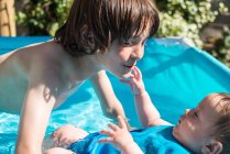 Felices hermanos jugando en la piscina inflable en el día de verano - foto de stock