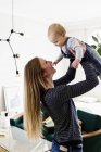 Woman holding up baby daughter in living room — Stock Photo