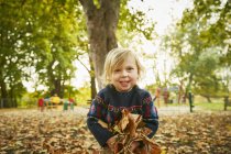 Souriante fille jouant dans les feuilles d'automne — Photo de stock