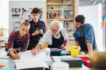Senior male craftsman brainstorming ideas with group of young men and women in book arts workshop — Stock Photo