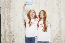 Retrato de hermanas gemelas con jerséis navideños, tomando selfie usando smartphone - foto de stock