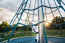 Portrait of boy in astronaut costume hiding and peering from playground climbing frame — Stock Photo