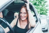 Portrait de jeune femme aux longs cheveux roux et taches de rousseur à la fenêtre de la voiture — Photo de stock