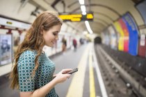 Seitenansicht einer Frau am Bahnsteig, die auf ihr Smartphone schaut — Stockfoto